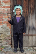 Niño con el disfraz de monstruo negro y el tocado verde delante de una puerta de madera