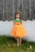 Niña de pie con vestido naranja de calabaza, falda de tul y diadema con hojas verdes.