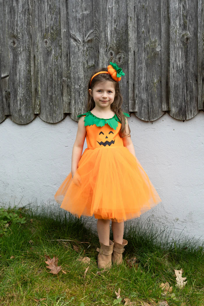 Niña de pie con vestido naranja de calabaza, falda de tul y diadema con hojas verdes.