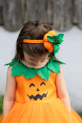 Detalle de la diadema con calabaza naranja y hojas verdes sobre el vestido con cara de calabaza.