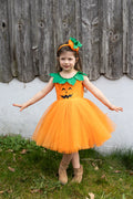 Niña con los brazos abiertos llevando vestido naranja de calabaza, falda de tul y diadema.