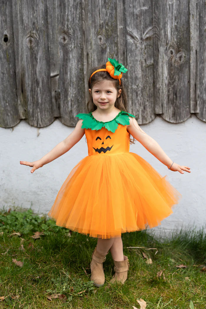 Niña con los brazos abiertos llevando vestido naranja de calabaza, falda de tul y diadema.