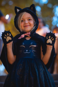 Niña con capucha de gato negro, lazo rosa y manos con patitas de gato en los bolsillos