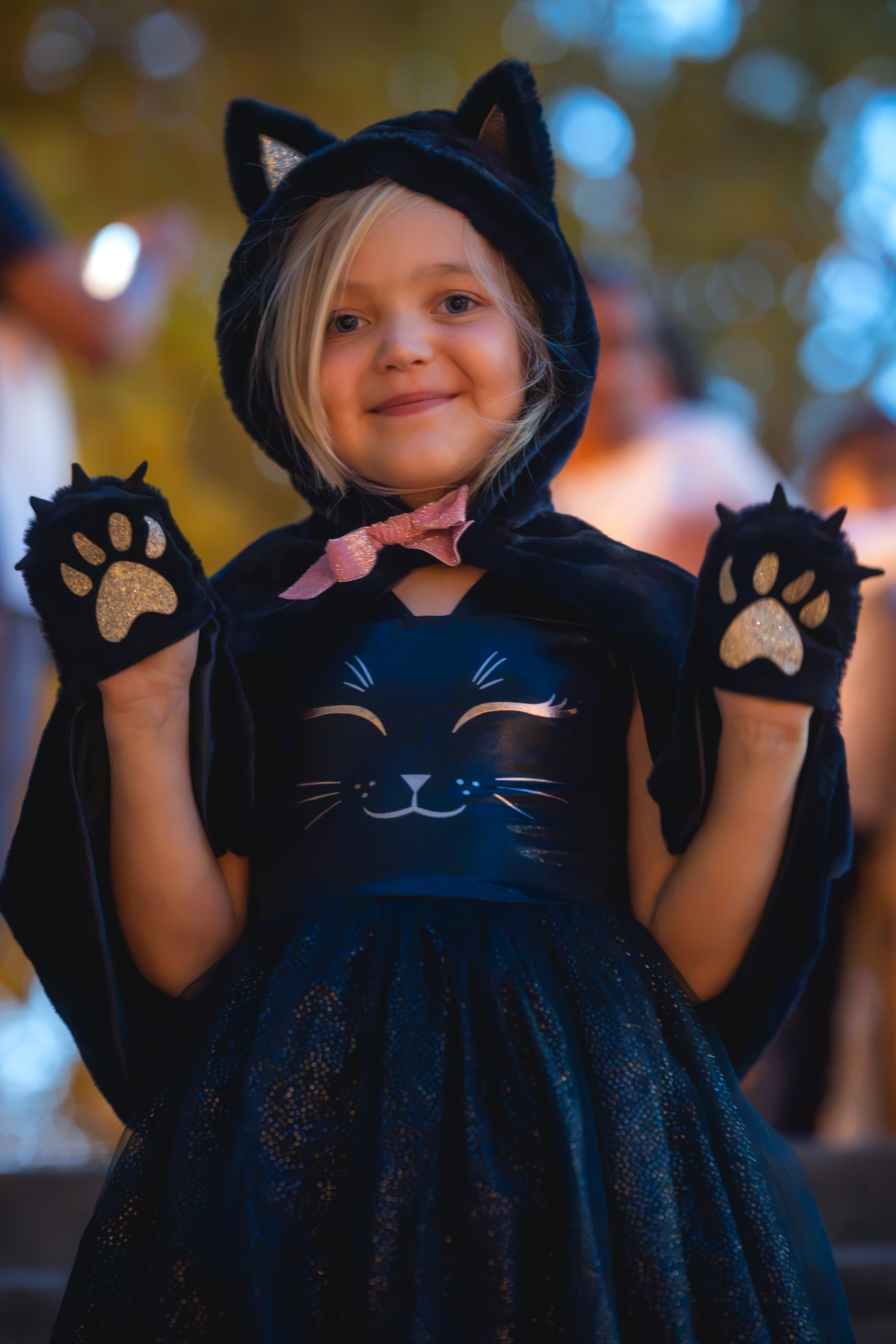 Niña con capucha de gato negro, lazo rosa y manos con patitas de gato en los bolsillos