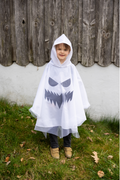 Niña pequeña con poncho blanco de fantasma con cara negra paseando por un jardín