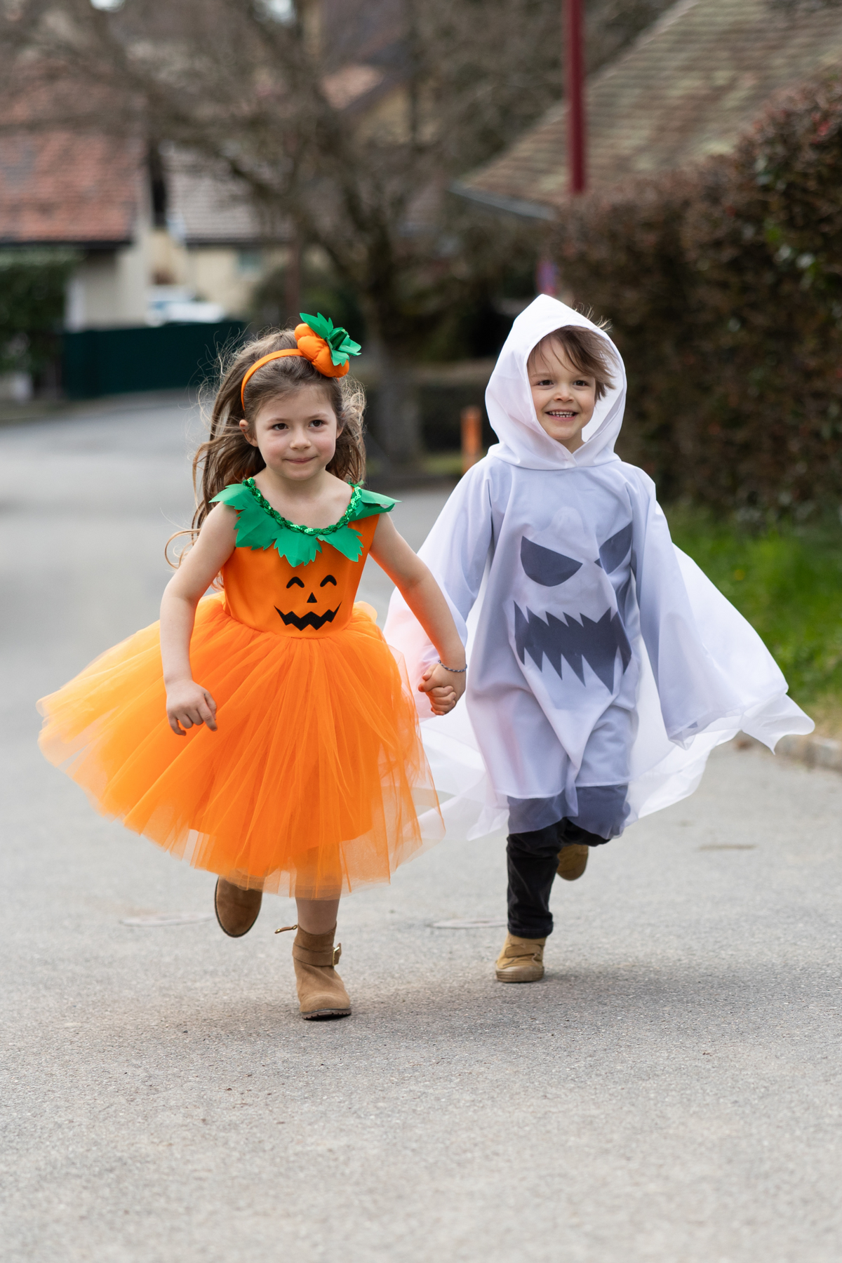 Dos niños corriendo por la calle, uno con el poncho de fantasma y otra con vestido naranja